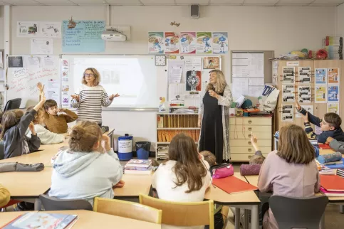Classe de primaire avec des enseignantes et des élèves qui lèvent la main pour interragir en classe